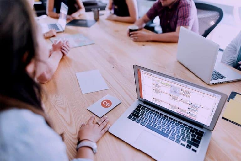 A group of people sitting around a table with laptops.